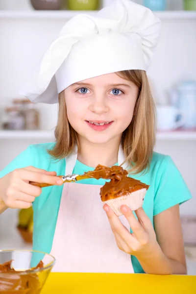 Menina pequena decorando cupcakes na cozinha em casa — Fotografia de Stock