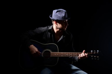 genç müzisyen akustik gitar çalıyor ve şarkı söyleme, koyu arka plan üzerinde
