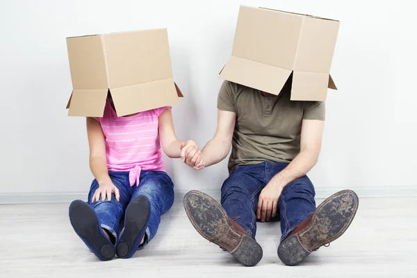 Couple with cardboard boxes on their heads sitting on floor near wall — Stock Photo, Image