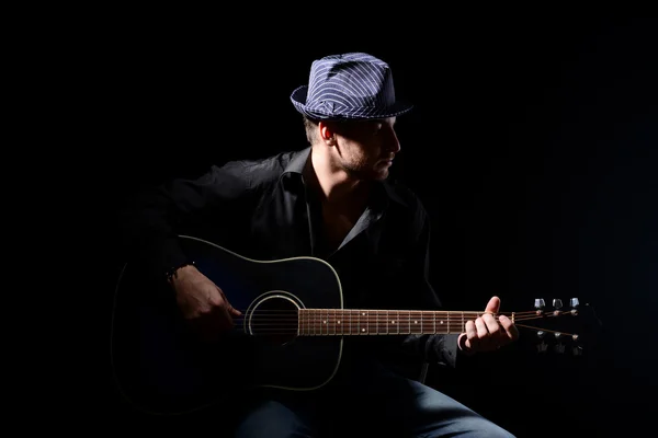 Young musician playing acoustic guitar and singing, on dark background — Stock Photo, Image