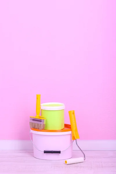 Paints, roll and paintbrush on floor in room on wall background — Stock Photo, Image