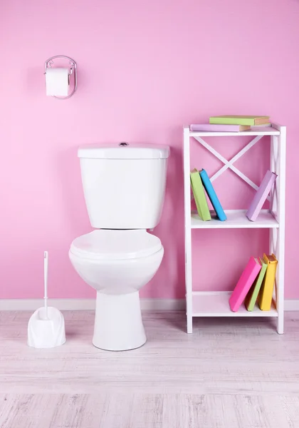 Weiße Toilettenschüssel und Ständer mit Büchern, auf farbigem Wandhintergrund — Stockfoto