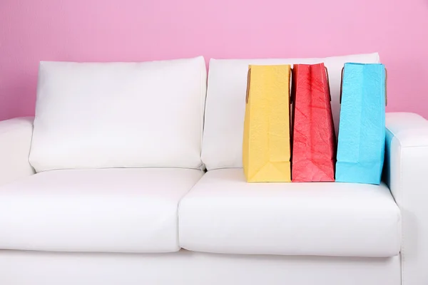 壁の背景の色のソファの上のカラフルなショッピング バッグ — ストック写真