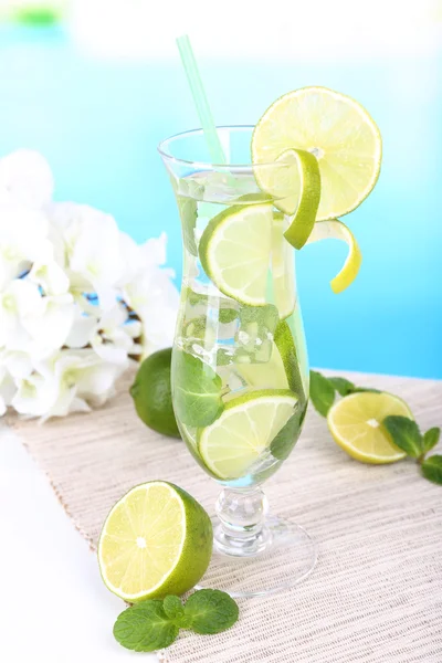 Bicchiere di cocktail con lime e menta sul tavolo su sfondo azzurro — Foto Stock