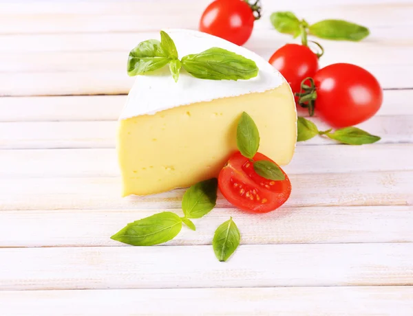 Tasty Camembert cheese with basil and tomatoes, on wooden table — Stock Photo, Image