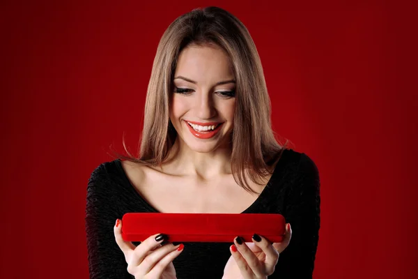 Girl looks at box with jewelry gift on color background — Stock Photo, Image