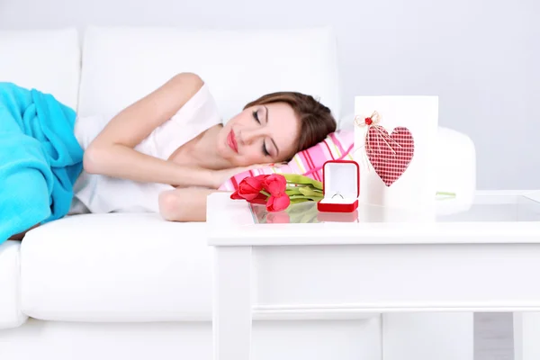 Piękna młoda kobieta śpi na kanapie w pobliżu tabela prezenty i kwiaty, z bliska — Stockfoto