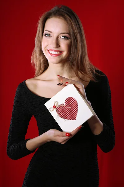 Mujer atractiva con postal, sobre fondo rojo —  Fotos de Stock