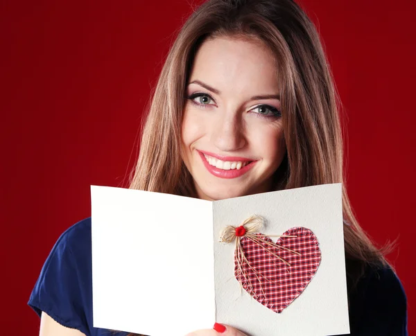 Aantrekkelijke vrouw met briefkaart, op rode achtergrond — Stockfoto