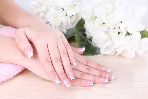 Belas mãos de mulher com manicure francês e flores na mesa de perto — Fotografia de Stock