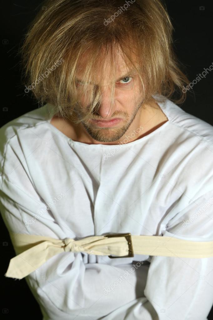 Mentally ill man in strait-jacket on black background