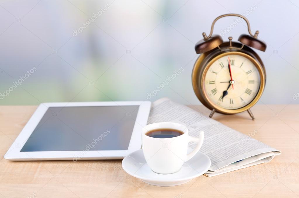 Tablet, newspaper, cup of coffee and alarm clock on wooden table
