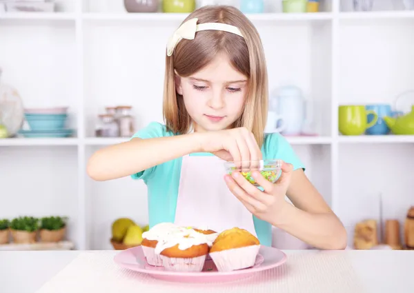 Liten flicka dekorera muffins i köket hemma — Stockfoto