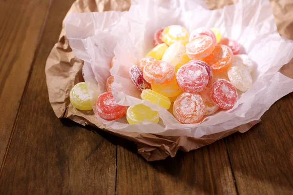 Sweet multicolor candies on paper, on wooden background — Stock Photo, Image