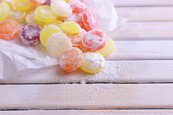 Słodkie cukierki multicolor na papierze, na tle drewniane kolor — Zdjęcie stockowe