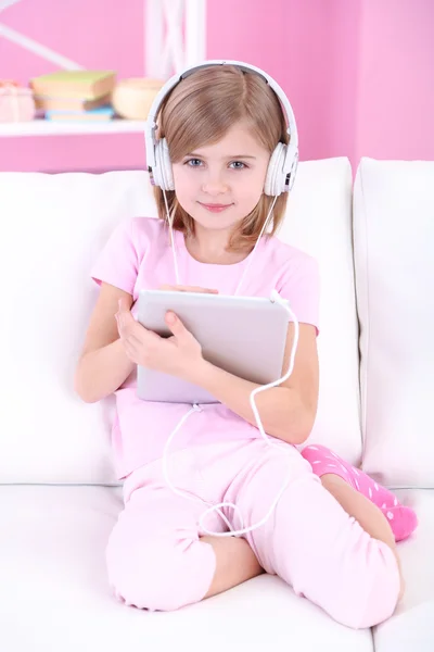 Little girl listening music sitting on sofa in room — Stock Photo, Image