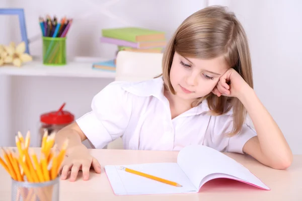 Little girl sitting at desk in room — Stock Photo, Image