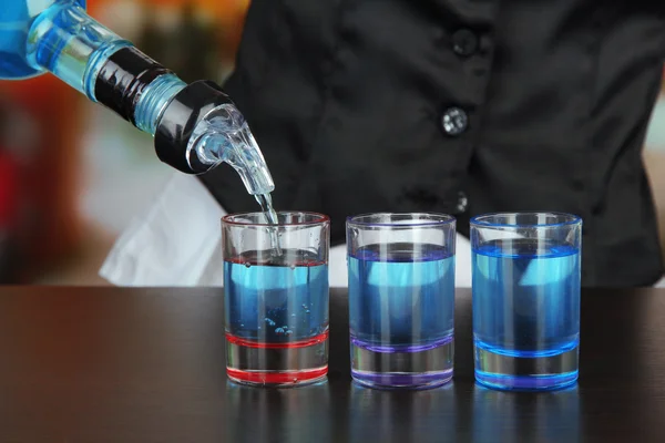 Barmen mão com garrafa derramando bebida em copos, no fundo brilhante — Fotografia de Stock