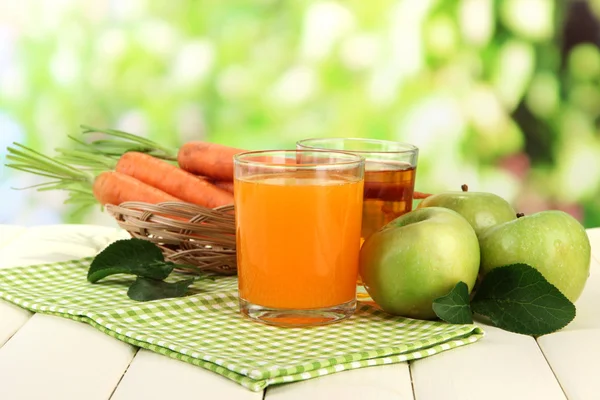 Glas juice, äpplen och morötter på vita träbord, på grön bakgrund — Stockfoto