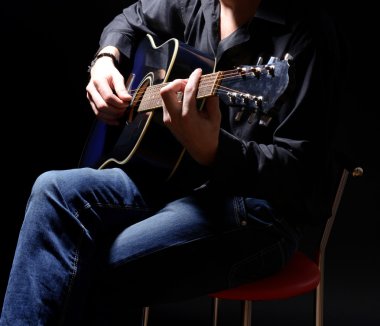 genç müzisyen akustik gitar çalıyor ve şarkı söyleme, koyu arka plan üzerinde