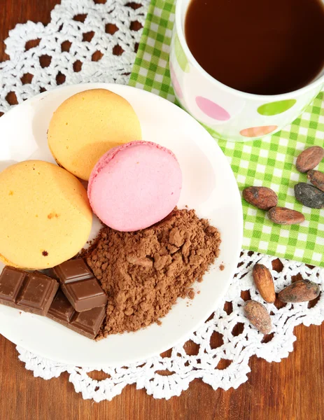 Cacao en taza con dulces y cacao en polvo en plato sobre mesa de madera —  Fotos de Stock