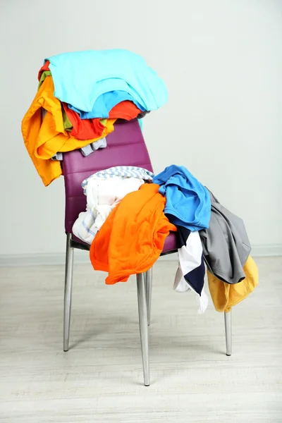 Heap of clothes on color chair, on gray background — Stock Photo, Image
