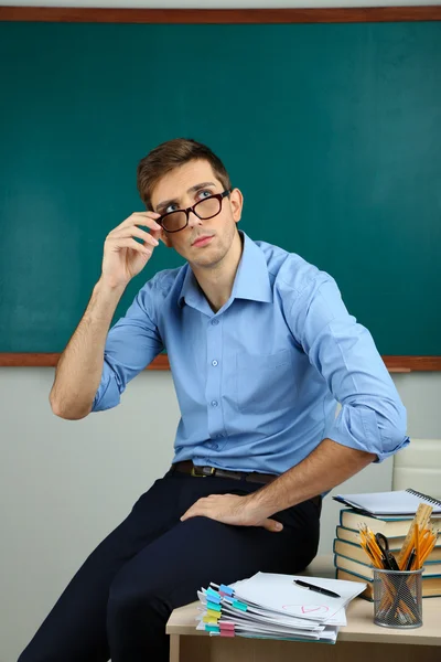 Young teacher sitting on desk in school classroom — Stock Photo, Image