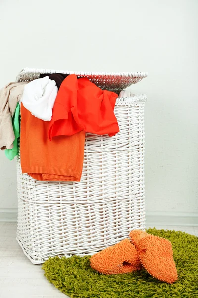 Cesta de ropa completa en alfombra de color sobre fondo de pared gris — Foto de Stock