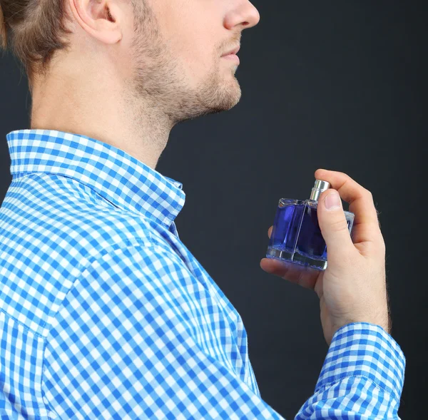 Bonito jovem usando perfume no fundo preto — Fotografia de Stock