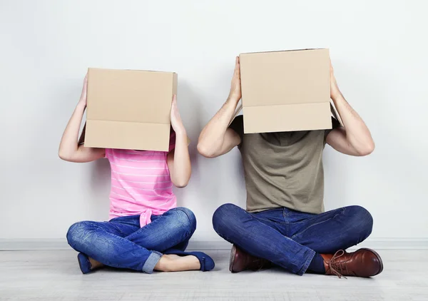 Couple with cardboard boxes on their heads sitting on floor near wall — Stock Photo, Image