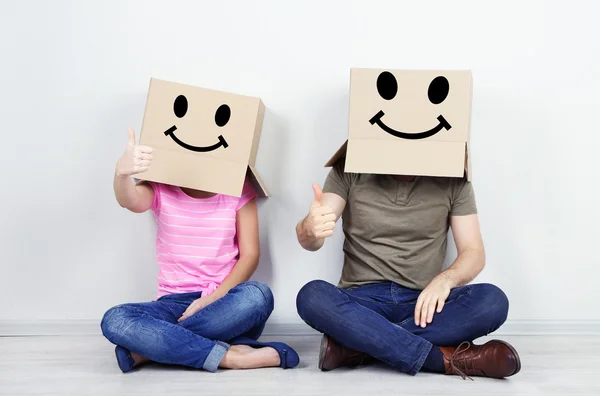 Paar mit Pappkartons auf dem Kopf sitzt auf dem Boden neben Wand — Stockfoto
