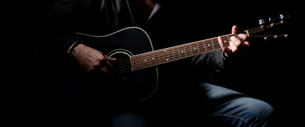 Young musician playing acoustic guitar and singing, on dark background — Stock Photo, Image