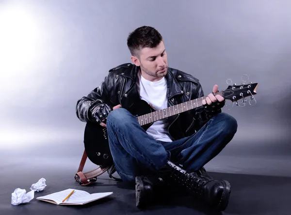 Młody muzyk gra na gitarze na szarym tle — Zdjęcie stockowe