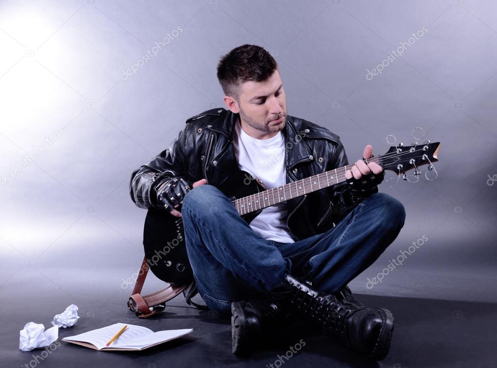 Young musician playing guitar on gray background