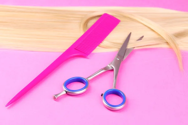 Długie blond włosy grzebieniem i nożyczki na różowym tle — Zdjęcie stockowe