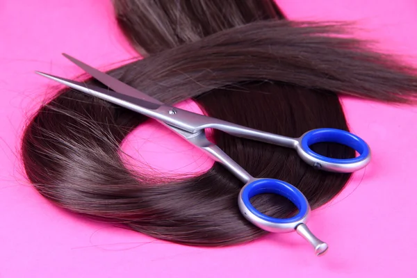 Long brown hair with scissors on pink background — Stock Photo, Image