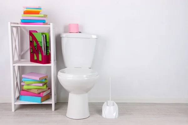 Tazón de inodoro blanco y soporte con libros, sobre fondo de pared de color — Foto de Stock