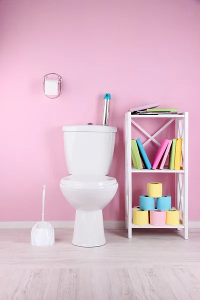 Tazón de inodoro blanco y soporte con libros, sobre fondo de pared de color — Foto de Stock