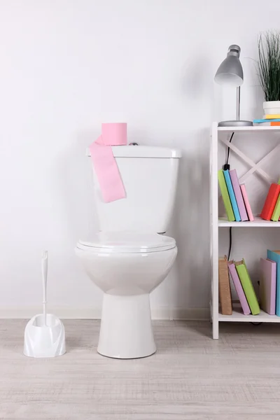 Weiße Toilettenschüssel und Ständer mit Büchern, auf farbigem Wandhintergrund — Stockfoto