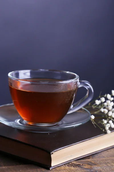Φλιτζάνι καυτό τσάι σε βιβλίο με λουλούδια στο τραπέζι σε γκρι φόντο — Φωτογραφία Αρχείου