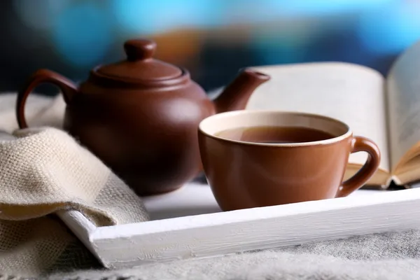 Taza de té caliente con tetera y libro en la mesa sobre fondo brillante —  Fotos de Stock