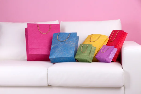 Divan, renkli duvar arka plan üzerinde renkli alışveriş torbaları — Stok fotoğraf