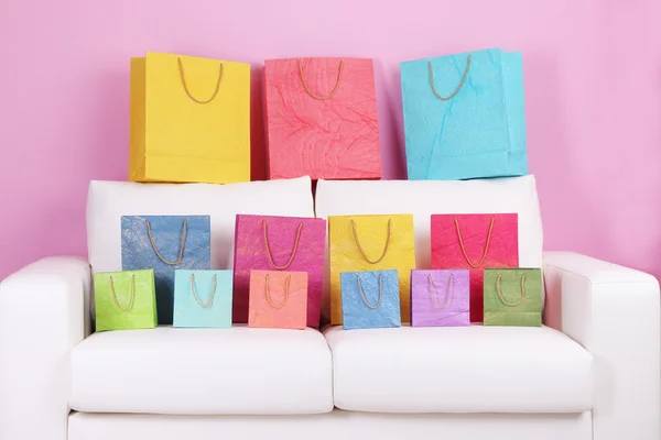 Barevné tašky na pohovku, na zeď na barvu pozadí — Stock fotografie