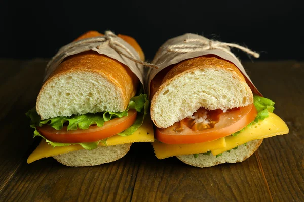 Sandwich fresco e gustoso su tavolo in legno su sfondo nero — Foto Stock