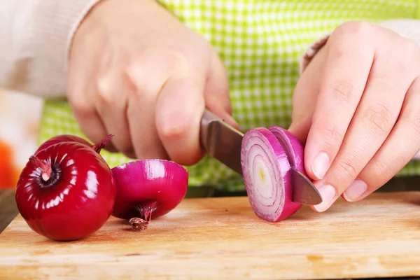 Female hands cutting bulb onion, on kitchen background — Stock Photo, Image