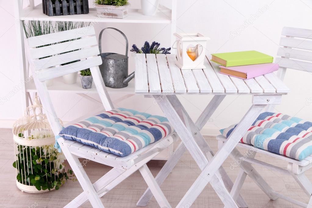 Garden chairs and table with flowers on shelves on white background