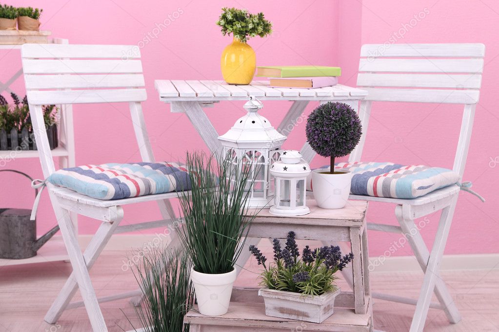 Garden chairs and table with flowers on shelves on pink background