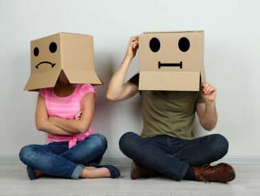 Couple with cardboard boxes on their heads sitting on floor near wall clipart