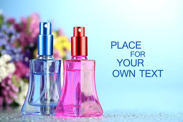 Women perfume in beautiful bottles and flowers on blue background