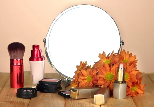 Round table mirror with cosmetics on table on beige background